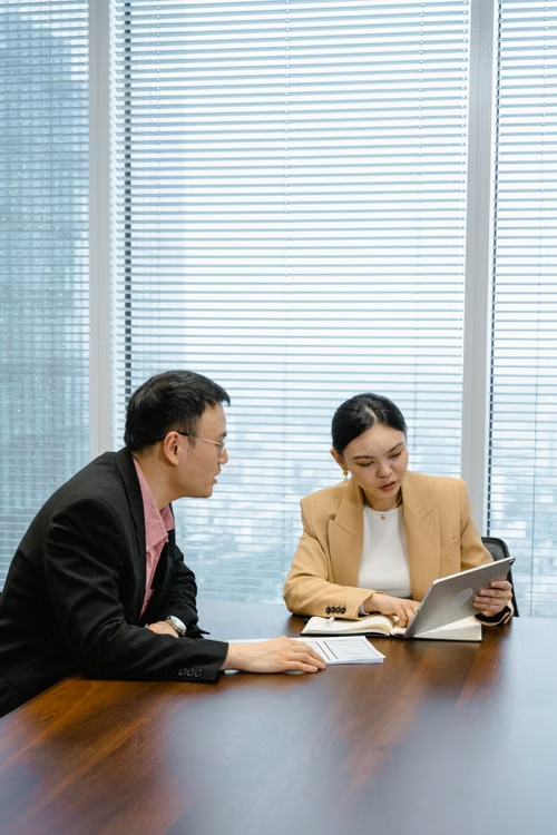 Two colleagues reviewing documents together at a meeting table in a high-rise office